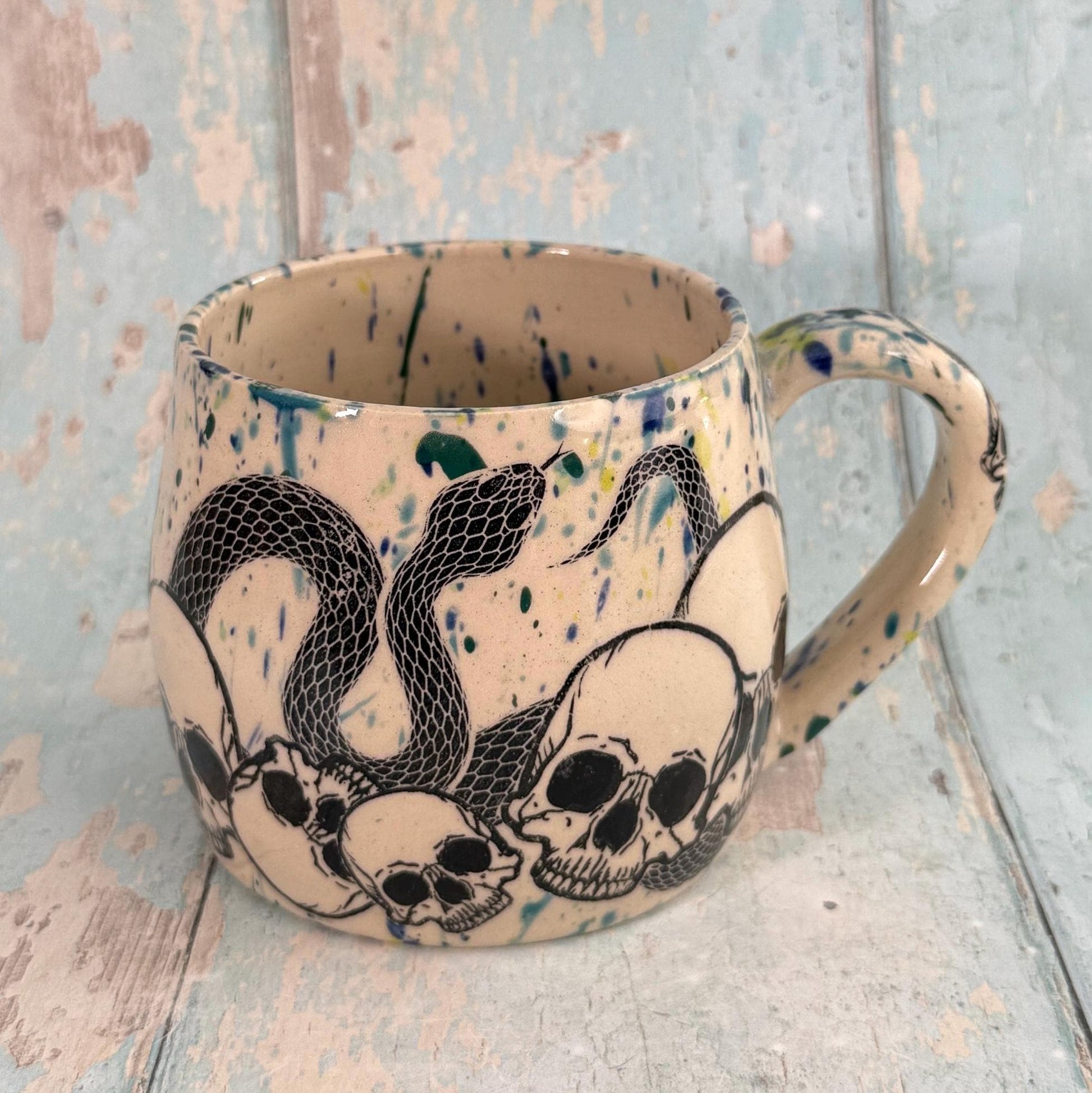 Ceramic mug with snake and skull design on a textured surface